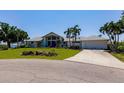 Charming one-story home featuring lush landscaping, palm trees, and a concrete driveway at 12439 Prather Ave, Port Charlotte, FL 33981
