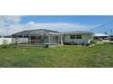 Backyard view of the home with a screened-in pool enclosure, lush lawn, and landscaping at 570 Mimosa Nw Ave, Port Charlotte, FL 33952