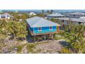 Beautiful blue elevated beach house showcasing wood decks, a metal roof, and lush tropical surroundings at 9390 Little Gasparilla Island, Placida, FL 33946