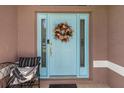 A welcoming light blue front door is decorated with a wreath and decorative side lights at 1327 Hedgewood Cir, North Port, FL 34288