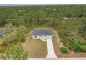 Areal view of a charming single-story home featuring a well-manicured lawn and long driveway in a wooded area at 27456 Corinthian Dr, Punta Gorda, FL 33955