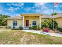 Inviting yellow home showcasing a landscaped yard, bright red door, and classic architectural details at 13325 Ketridge Ave, Port Charlotte, FL 33953