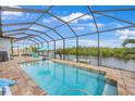 Screened-in pool with a view of the water, lounge chairs, and a clear blue sky at 19246 Moore Haven Ct, Port Charlotte, FL 33948