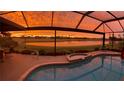 Screened pool with sunset view of golf course and pond, enhanced by stunning orange and yellow sky at 5461 White Ibis Dr, North Port, FL 34287