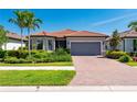 Inviting single-story home with a red tile roof, brick driveway, manicured landscaping, and a two-car garage at 1470 Hyssop Loop, North Port, FL 34289