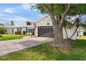 Beautiful home with a brick driveway, a gray two-car garage, and lush green lawn under a tree at 425 Corrientes Cir, Punta Gorda, FL 33983