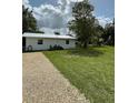 A single-story home featuring a gravel driveway, set against a backdrop of a large grassy lot and mature trees at 5727 Beechwood St, Punta Gorda, FL 33982