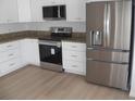 Modern kitchen featuring stainless steel appliances, white cabinets, granite countertops, and wood grain flooring at 23167 Turnbull Ave, Port Charlotte, FL 33954