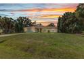 Charming single-story home featuring a well-maintained lawn, mature trees, and inviting curb appeal against a colorful sunset at 3305 Nansen Ln, North Port, FL 34286