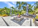 Outdoor stone patio with a cozy fire pit, lounge chairs, and bench seating surrounded by lush tropical landscaping at 25062 Palisade Rd, Punta Gorda, FL 33983