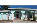 Light blue home featuring a charming arched entry, double red doors, and lush landscaping at 39 Norman St, Port Charlotte, FL 33954