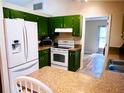 A kitchen features green cabinets, beige countertops, tile flooring, and stainless steel appliances at 15090 Rebecca Ave, Port Charlotte, FL 33953