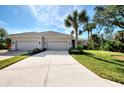 Tan two-car garage villa with a tile roof, palm trees, and a nicely landscaped lawn at 14311 Reserve Ct, Port Charlotte, FL 33953