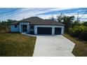 Beautiful modern home featuring a two-car garage, lush lawn and a stylish front entrance with a beautiful blue sky at 7330 Printer St, Port Charlotte, FL 33981