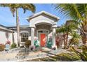 Charming home entrance featuring a vibrant coral door, inviting chairs, and lush landscaping at 13354 Blytheville Ave, Port Charlotte, FL 33981