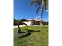 Charming pink single-story home featuring a well-maintained lawn, palm trees, and a two-car garage at 14244 Spruce Ln, Port Charlotte, FL 33953