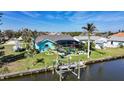 Waterfront home featuring a boat lift, lush landscaping, and a screened-in pool area at 15652 Ruston Cir, Port Charlotte, FL 33981
