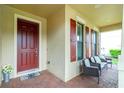 Covered front porch offering stylish seating and a red front door, complemented by a red brick floor at 2628 Sherman Oak Dr, North Port, FL 34289