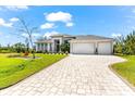 Beautifully landscaped front yard leading to a modern home with a three-car garage and a paver driveway at 10491 Sarasota Rd, Port Charlotte, FL 33981