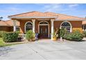 Charming home exterior featuring a terracotta tile roof, columned entryway, and meticulously landscaped front yard at 103 Mecca St, Port Charlotte, FL 33954