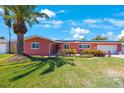 Charming coral home featuring a two-car garage, lush lawn, solar panels, and tropical landscaping at 1694 Harbor W Cir, Largo, FL 33770