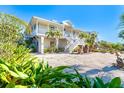 Two-story coastal home with white exterior, palm trees, large yard with rock groundcover and stairway to the front door at 62 Tarpon Way, Placida, FL 33946