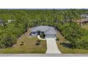 A well-manicured lawn with a newly built gray home with mature landscaping and a long driveway at 15613 Alsask Cir, Port Charlotte, FL 33981