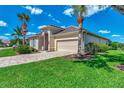 Attractive home with a stone driveway, two-car garage, well-maintained lawn, and lush, mature palm trees at 13335 Golf Pointe Dr, Port Charlotte, FL 33953