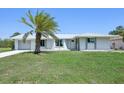 Inviting home exterior featuring a mature palm tree, metal roof, and a well-kept lawn under a clear blue sky at 3246 Yukon Dr, Port Charlotte, FL 33948