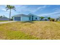 Exterior elevation of a light blue home featuring a two-car garage, palm tree, and lawn at 12359 Deepwoods Ave, Port Charlotte, FL 33981