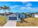 Exterior elevation of a one-story light blue home featuring a two-car garage, palm tree, and a well-manicured lawn at 12359 Deepwoods Ave, Port Charlotte, FL 33981