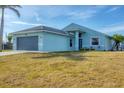 Exterior elevation of a light blue home with a two-car garage and lawn with a palm tree at 12359 Deepwoods Ave, Port Charlotte, FL 33981
