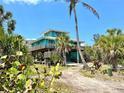 Two-story beach house with a wooden deck surrounded by lush greenery, blending nature and home at 9580 Almirate Ct, Placida, FL 33946