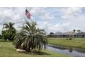 Picturesque backyard view with American flag, canal, mature palms, and neighboring screened lanais at 169 Fairway Rd, Rotonda West, FL 33947