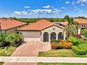Charming single-story home featuring a red tile roof, arched entryway, lush landscaping, and a brick-paved driveway at 23590 Copperleaf Dr, Venice, FL 34293