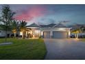 Charming single-story home with a three-car garage, brick driveway, and manicured lawn under a vibrant sunset sky at 15176 Spanish Point Dr, Port Charlotte, FL 33981