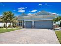 Inviting single-story home featuring a three-car garage, brick driveway, and verdant lawn under clear blue skies at 15176 Spanish Point Dr, Port Charlotte, FL 33981