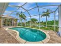 Inviting screened-in pool area with brick patio and view of the water and tropical landscaping at 29 Tournament Rd, Rotonda West, FL 33947