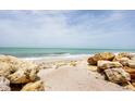 A beachside view of rocks, sand, and gentle ocean waves under a clear sky, inviting relaxation at 7420 Manasota Key Rd, Englewood, FL 34223