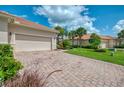 Long brick driveway leading to an attached garage with lush landscaping and blue skies at 13051 Creekside Ln, Port Charlotte, FL 33953