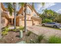 Inviting townhome exterior featuring a multi-car garage, brick driveway, and tropical landscaping including palms at 8228 Villa Grande Ct, Sarasota, FL 34243