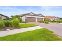 Villa exterior featuring a two-car garage, brick driveway, manicured lawn, and decorative plants at 10258 Morning Mist Ln, Sarasota, FL 34241