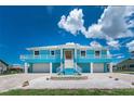 The raised two-story home offers a symmetrical design, blue exterior, a white railing, and a crushed shell ground cover at 1930 Massachusetts Ave, Englewood, FL 34224