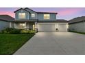 Charming two-story home featuring a three-car garage, covered porch, and beautifully landscaped front yard at dusk at 11728 June Briar Loop, San Antonio, FL 33576