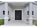 Close up of front of home with gray exterior, black double doors, covered porch area, and lush green grass at 14 S Forest St, Plant City, FL 33563