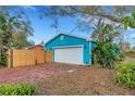 Blue garage with a white door and brick parking, surrounded by lush foliage and a wooden fence at 1000 Michigan Blvd, Dunedin, FL 34698