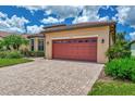 Tan house with red garage door, lush landscaping, and paved driveway at 20193 Pezzana Dr, Venice, FL 34292