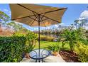 Relaxing outdoor patio with a table, umbrella, and serene view of the lush landscape and pond at 804 Montrose Dr # 103, Venice, FL 34293