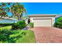 Tan house with a two-car garage and brick driveway. Lush landscaping at 9028 Coachman Dr, Venice, FL 34293