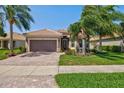 Front exterior view of a house with a two-car garage, palm trees, and flowers in the garden at 19225 Jacinda St, Venice, FL 34293